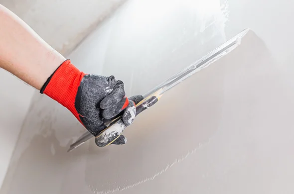 Close-up of a worker using a drywall sander to smooth a wall, representing expert commercial drywall repair services.