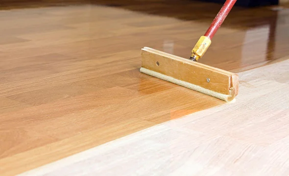 Close-up of a roller applying finish to a hardwood floor, showcasing expert floor refinishing and restoration services.