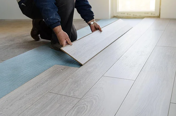 Worker using tools to install hardwood flooring on a neatly prepared surface, showcasing expert hardwood flooring installation.