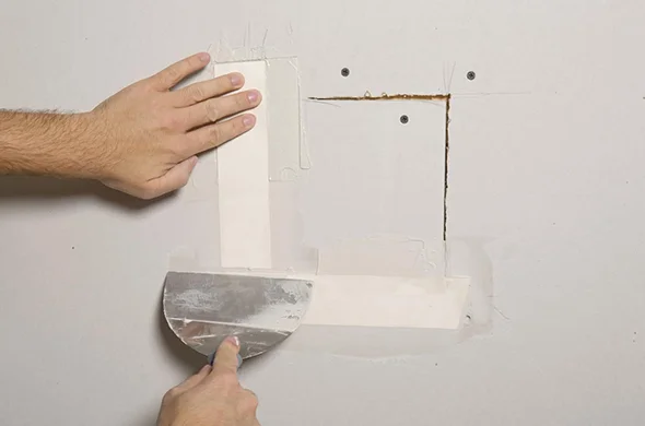 Close-up of a hand using a drywall knife to apply joint compound on a wall, showcasing precise residential drywall repair services.