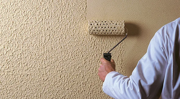 Hand applying a textured finish to a drywall surface, representing professional wall finishing services.