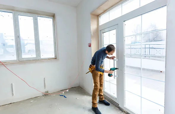 Construction worker measuring and preparing for window and door replacement in a home, representing professional remodeling services.